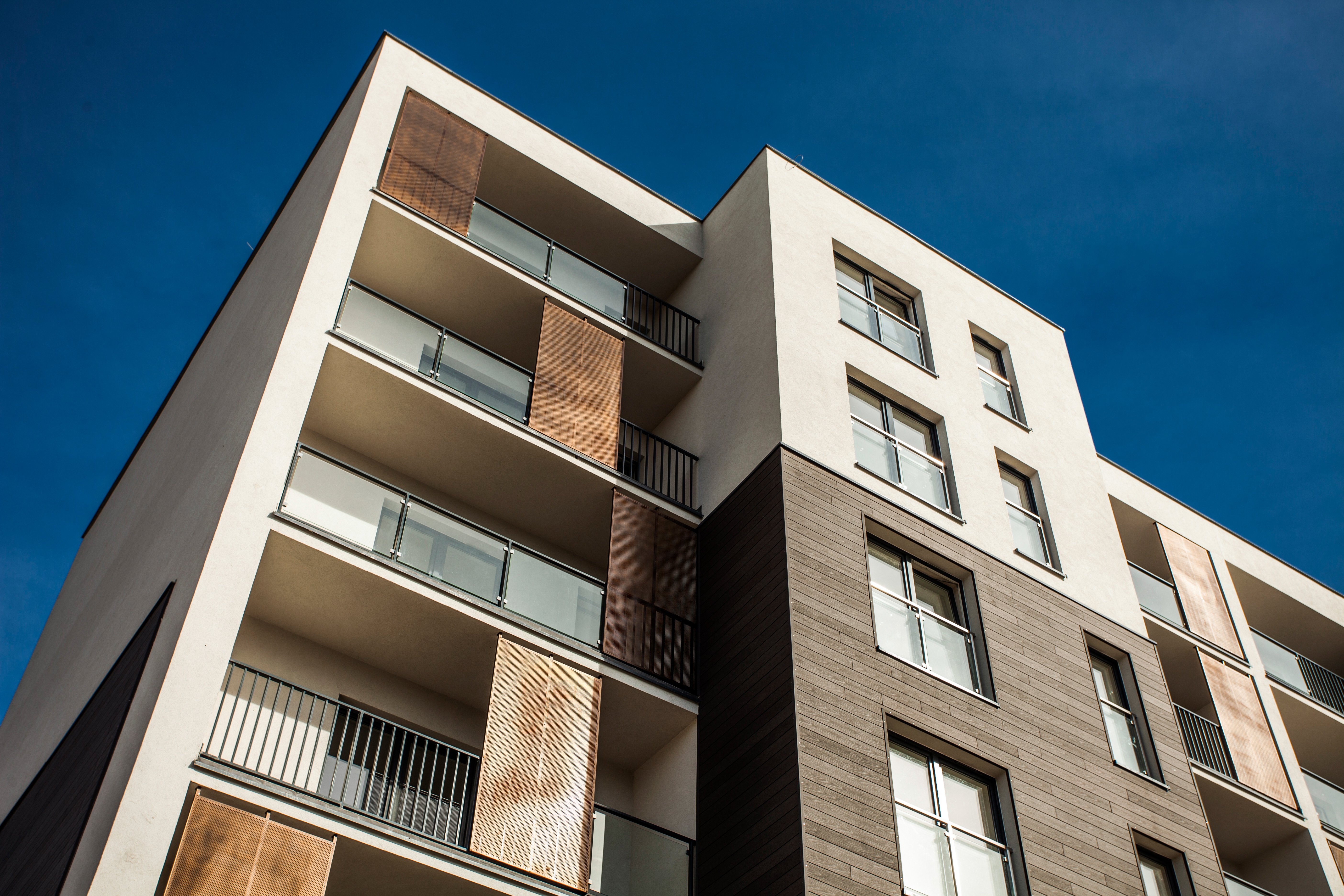 Modern multi-storey modular residential building with balconies and a mix of light and dark façade materials, photographed against a clear blue sky.